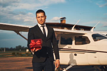 Stylish young man with gift box standing at airdrome