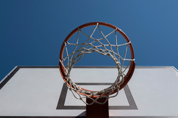 Basketball hoop on outdoor basketball court with blue sky background. Low angle view