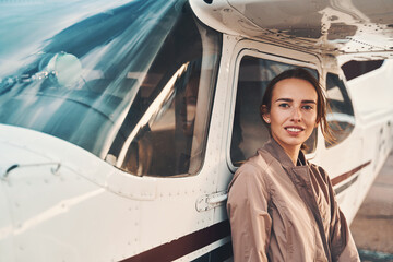 Cheerful young woman standing near airplane at airdrome