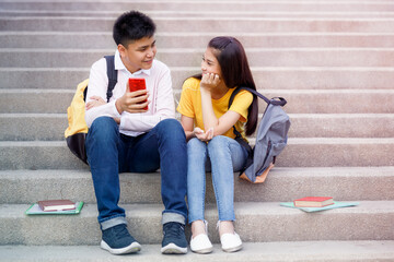 asian teenagers friendship sitting on stair in the garden and looking mobile phone