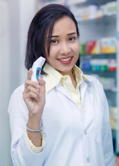 Asian woman pharmacist with digital thermometer standing in pharmacy drugstore