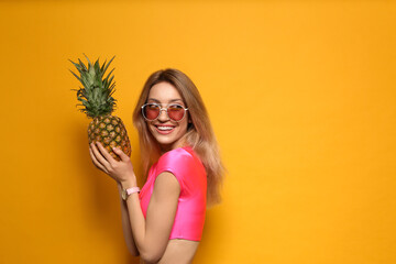 Young woman with fresh pineapple on yellow background, space for text. Exotic fruit