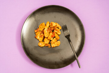 Black plate of Gnocchi with red sauce on a purple table. Accompanies a modern black fork.