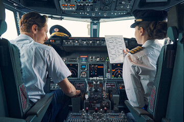 Pilot and female first officer seated in the flight deck - obrazy, fototapety, plakaty