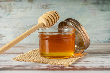 Jar of pure honey from bees with the wooden honey stick resting on the jar on a rustic table.