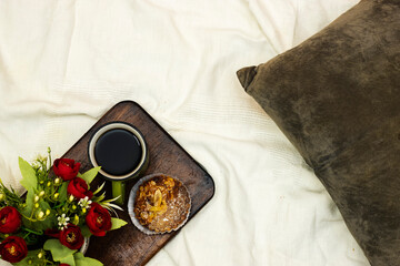 cup of hot coffee with almonds pie, flowers pot and pillow on white bed background, vintage tone, top view. Lifestyle concept