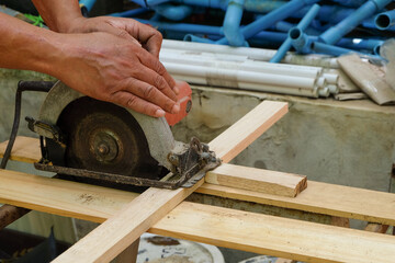 A carpenter is sawing wood with a circular saw.