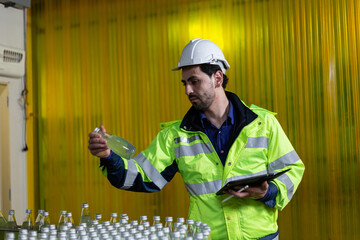 Male factory manger using digital tablet checking information and quality control for juice drink product on bottling factory machinery. Process of beverage industrial production