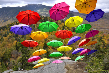 Fototapeta na wymiar Unexpected and whimsical autumn scene featuring airborne parasols. Attention-grabbing image of colorful umbrellas soaring skyward over scenic Franconia Notch in White Mountains of New Hampshire.