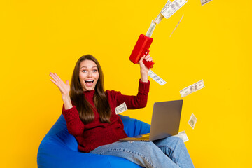 Photo of amazed brunette happy young woman hold laptop sit chair money fall wear jeans isolated on...
