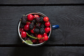 cherries and mulberries in a cup on a black wooden table scattered, fruit background, fruit
