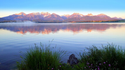 Morgenstimmung am Hopfensee im Allgäu im rötlichen
Morgenlicht auf den Bergen am stillem See