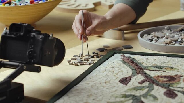 Male hands create mosaics floral pattern using tweezers and small pieces of granite stone. Master making handicraft in a creative workshop. Interesting hobby, art, work of art. Close up. Slow motion.