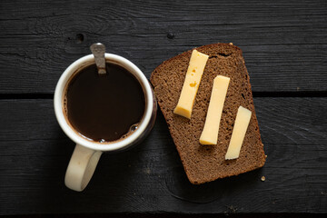 a cup with black coffee and a slice of bread with hard cheese on a black wooden table, homemade coffee for breakfast