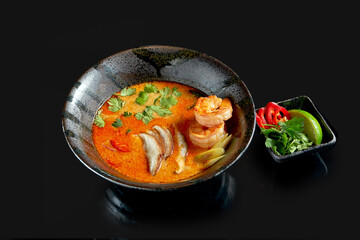 Asian tom yum soup with shrimps, shiitake mushrooms, octopus, tomatoes and rice in a plate. Classic Asian cuisine. Food delivery. Isolated on black