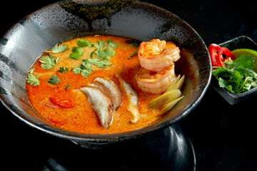 Asian tom yum soup with shrimps, shiitake mushrooms, octopus, tomatoes and rice in a plate. Classic Asian cuisine. Food delivery. Isolated on black
