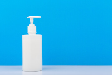Shower gel or liquid soap in white unbranded tube with dispenser on white  shelf against light blue wall with copy space. Concept of hygiene and moisturizing or relaxing shower gel