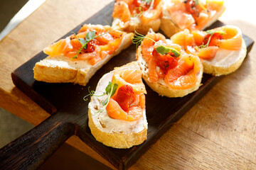 A red fish sandwich decorated with fresh herbs on a brown wooden board.