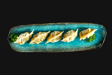 Mouth-watering Asian gyoza stuffed with seafood, served on a blue plate. Japanese Jiaozi or dumplings isolated on black background. Pan-Asian cuisine