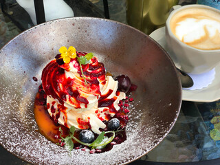 Beautifully decorated and delicious Pavlov's cake with berry sauce on a silver plate and cappuccino