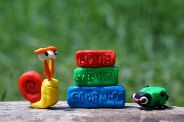 Fototapeta premium Toy snail and ladybug made of plasticine close-up. Next to the inscription love, happiness, good luck.