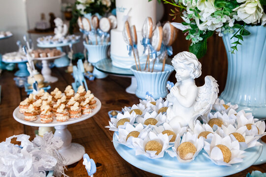 Decora&ccedil;&atilde;o da mesa do bolo de festa de batismo e anivers&aacute;rio de menino com muitos doces diferentes, com tema de cavalinhos e anjinhos nas cores azul e branco.