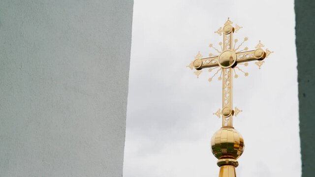 Religion and faith concept, bottom view of a golden cross of the church. Video. Big golden cross on cloudy sky background.