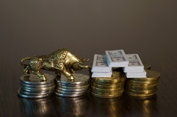 Metal bull with coins close-up on the table. Next to the bundles of dollars. Business concept.