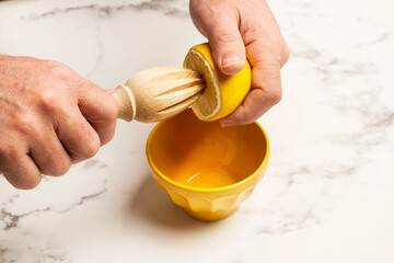 Manos de hombre exprimiendo un limón junto a un cuenco de cerámica amarillo sobre un fondo de...