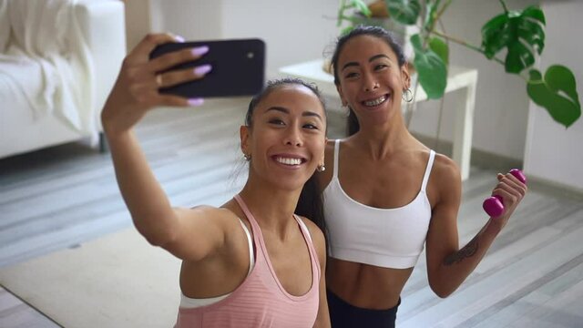 Female athletes posing and taking selfie photo during fitness training at home interior.