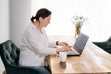 Middle age woman freelancer is working at home. Pretty plus size female in 40s working with laptop...