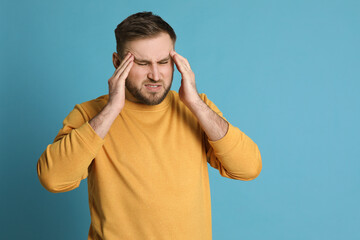 Fototapeta premium Man suffering from migraine on light blue background, space for text