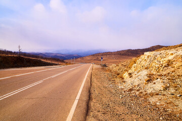 View of the old road with markings on an autumn day or evening and hills along the roadsides