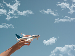 Boy's hand holding a model plane, airplane on a blue sky with some clouds.