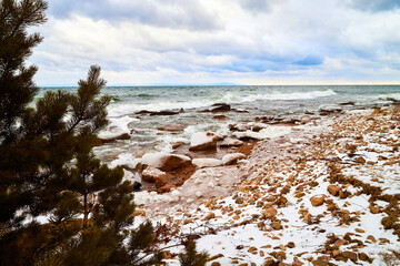 Nature landscape with dramatic sky and clouds, lake with ice, shore with snow and dark trees in...