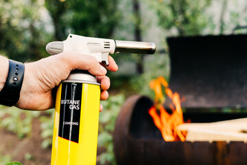 Close up man holds a gas burner with a balloon and makes a fire in the grill. Flame gun on the...