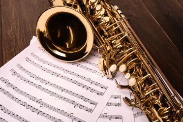 Beautiful saxophone and note sheets on wooden background, closeup