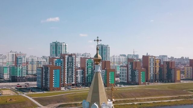Religion and faith concept, aerial view of a golden cross on the top of the church. Video. Big golden cross on colorful houses and cloudy blue sky background.