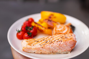 Hand holding plate of salmon fillet steak with cherry tomatoes and bell pepper. 