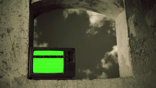 Vintage TV On Window Old Film Effect Television Green Screen. Vintage television with green screen on a big window with a cloudy sky in the background. Sepia old film effect