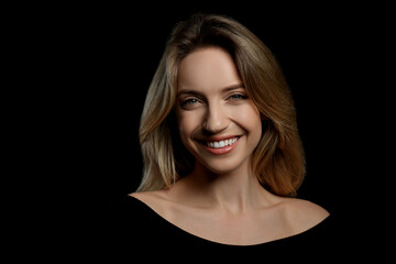 Portrait of happy young woman with beautiful blonde hair and charming smile on black background