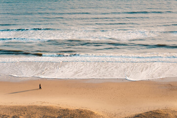 High angle shot of a couple and a  beautiful wavy ocean against a brown sand

