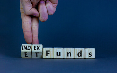 Index funds vs ETF symbol. Businessman turns a cube and changes words 'ETF, Exchange-Traded Fund' to 'Index funds. Beautiful grey background, copy space. Business and ETF vs index funds concept.