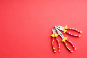 Technician's set of pliers on solid coloured red background including pliers, long nose pliers and cutters