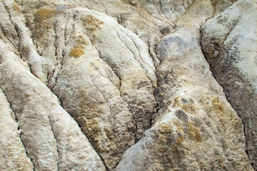 Close-up of a hillside made of gray-yellow clay. Curved surface folds, erosion results and cracks. Lifeless and desolate landscape. Image for texture or background.