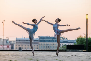 Two young ballerinas dancing in pointe shoes in city against the backdrop of sunset sky