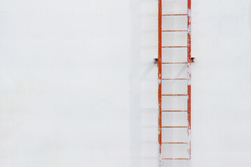 A red, metal, fire escape, smeared with white paint and casting a shadow against the background of a white plastered wall, is located vertically and to the right. Background and copy space.