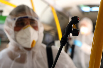Public transport sanitation. Worker in protective suit disinfecting bus salon, focus on spray machine nozzle
