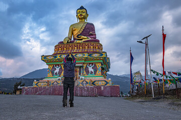 man praying at isolated huge buddha golden statue with moody sky at evening