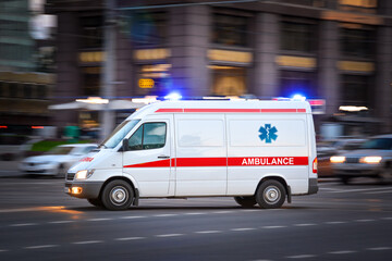 Ambulance Van on a wide city street. White emergency vehicle with warning lights and siren moving fast an avenue. Metropolis rescue services transport. Motion blur and selected focus